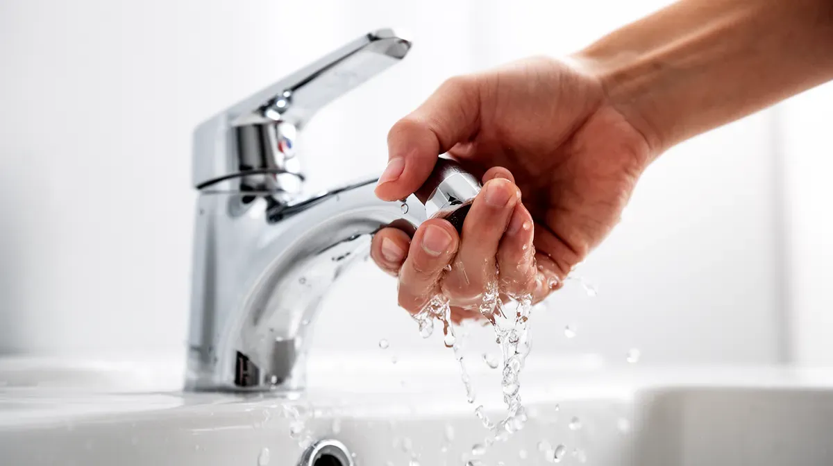 Gros plan sur une main ouvrant un robinet avec des gouttes d'eau, illustrant la consommation d'eau