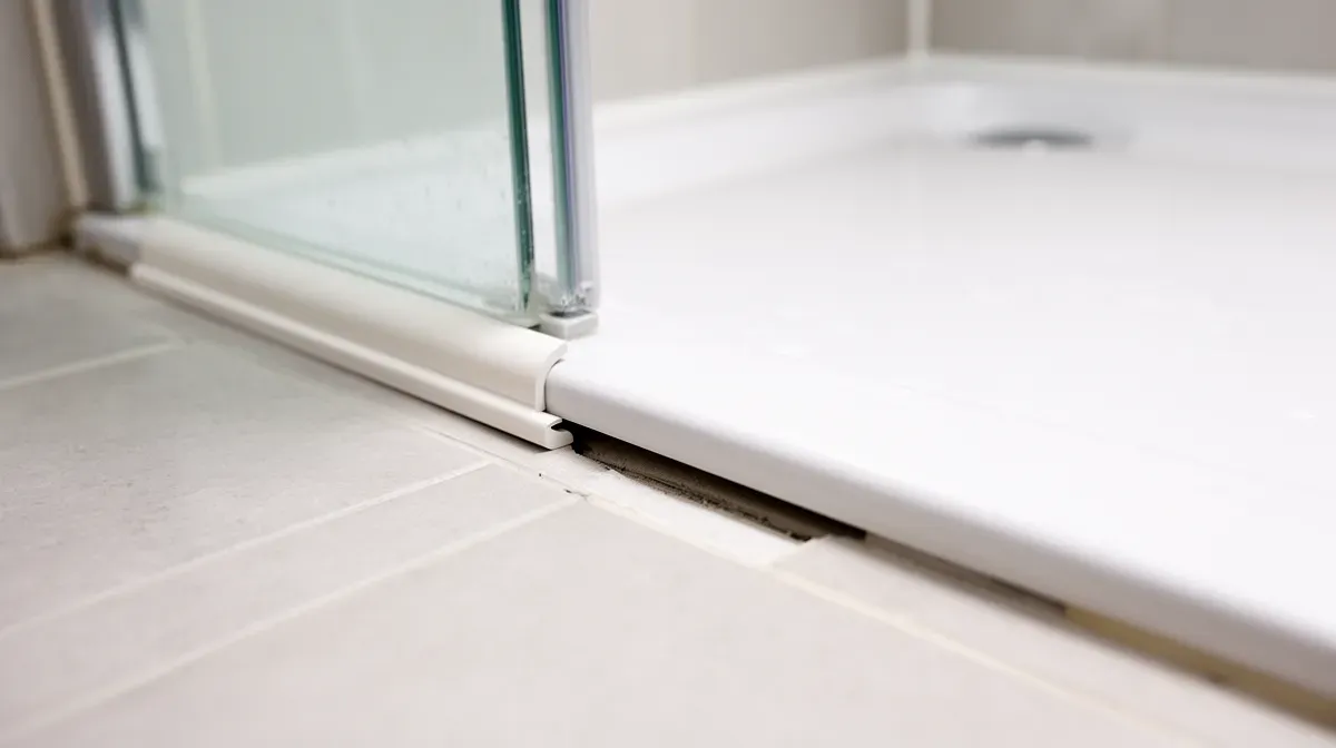 Installation d'une baguette quart-de-rond en PVC pour combler un espace de 15 à 25 mm sous un receveur de douche