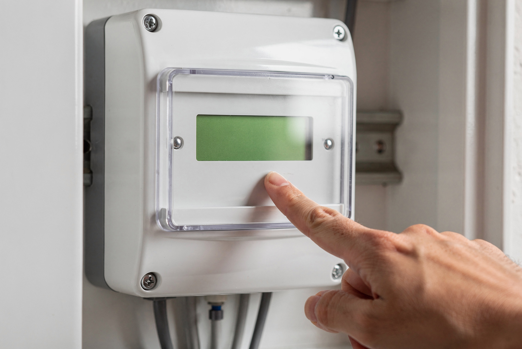 Compteur électrique communicant dans un tableau domestique, un doigt désignant l'écran de relevé de consommation