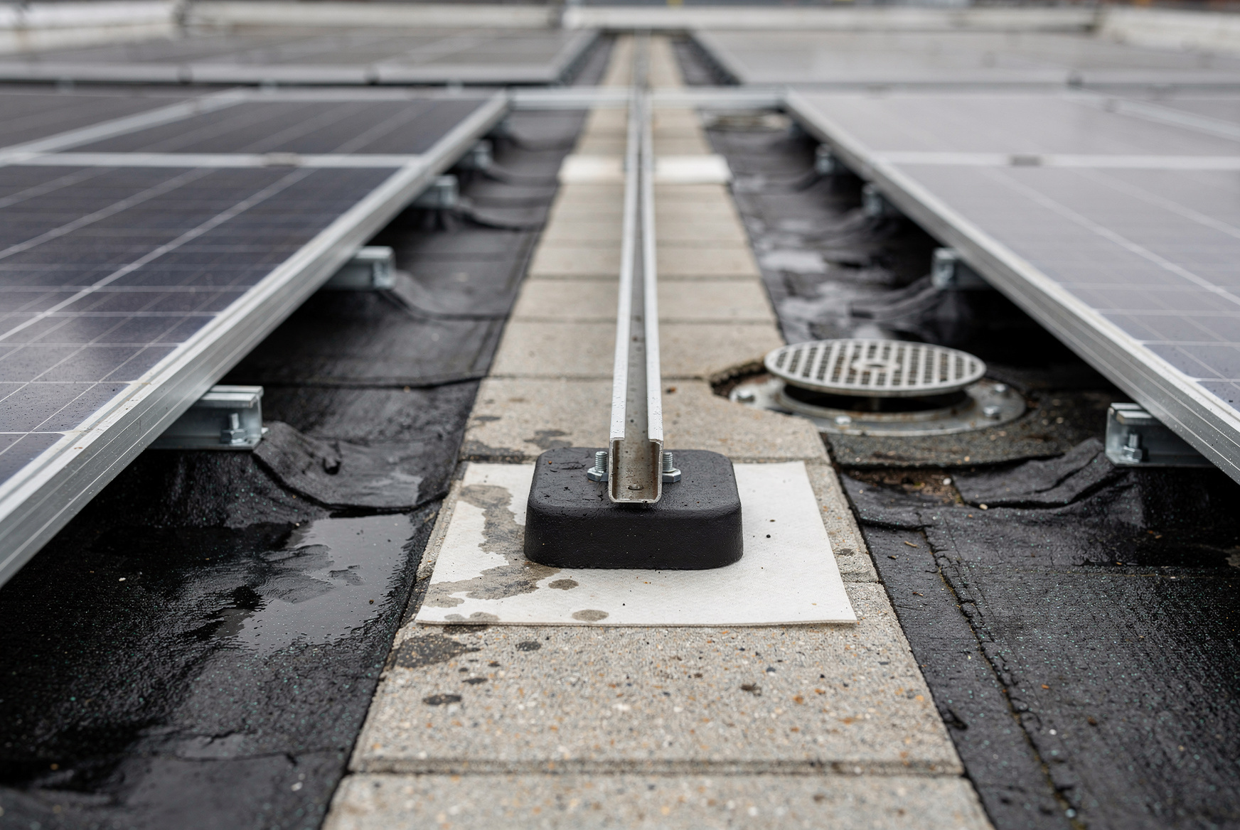 Plot de fixation non perforant posé sur une natte de protection et sur la membrane d'étanchéité, chemin de circulation en dalles et évacuation d'eau pluviale entre deux rangées de panneaux